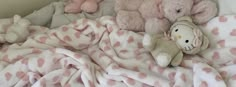 several stuffed animals are laying on a blanket in a bed with pink polka dot sheets