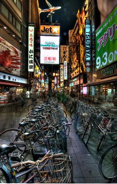 there are many bicycles parked on the sidewalk in front of buildings and billboards at night