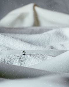 a small penguin standing in the snow on top of some white sheets and cloths