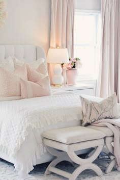 a white bed sitting next to a window covered in pink and white pillows on top of a rug