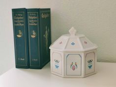 two books are sitting on a shelf next to a small white box with blue trim