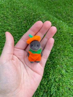 a hand holding a tiny stuffed animal with an orange hat and green scarf on it's head