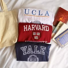 three t - shirts are laid out on a bed with books and an open book bag