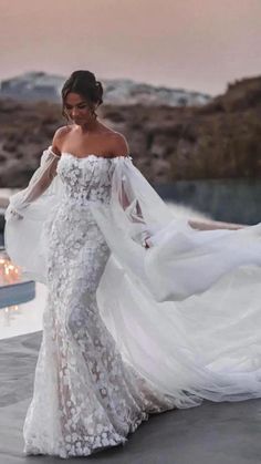 a woman in a white wedding dress is standing near a pool with candles on it