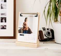 a wooden frame with a calendar on it next to a camera and potted plant