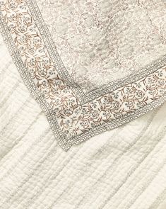 a close up view of a white quilt with brown and beige designs on it's edges