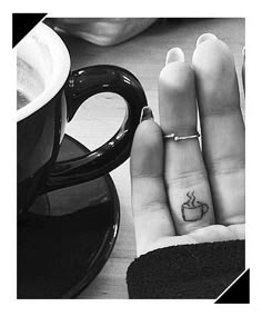 two fingers with small tattoos on them next to a coffee cup