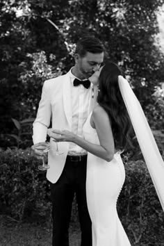 a bride and groom kissing in front of some bushes with their arms around each other