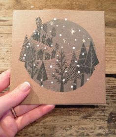 a hand holding up a card with trees and snowflakes in the sky on it