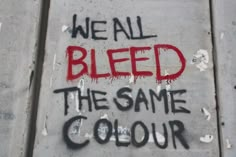 we all bleed the same color graffiti on a concrete wall that reads, we all bleed the same color