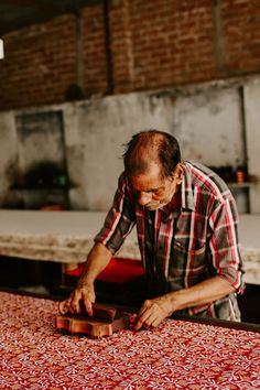 an old man is working on something in his workshop with red and white table cloth