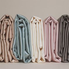 five different colored shirts lined up next to each other on a white surface with one folded in the middle