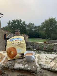 a cup of coffee sitting on top of a stone wall next to a bag of macaroni