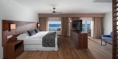 a hotel room with a bed, television and balcony overlooking the ocean in front of it