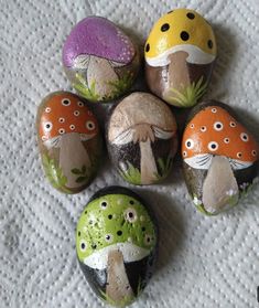 five painted rocks sitting on top of a white towel next to each other with different colored mushrooms