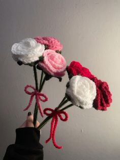 a hand holding a bunch of crocheted flowers with red, white and pink ribbons