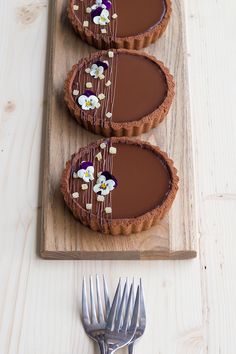 three chocolate tarts with white flowers on them and a fork next to the tart