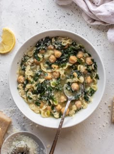 a white bowl filled with pasta and spinach next to sliced lemons on a table