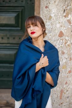 a woman wearing a blue shawl standing next to a stone wall with her hands on her chest