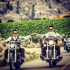 two men riding motorcycles on a road with trees in the background