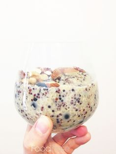 a hand holding a wine glass filled with pudding and nuts on the bottom, in front of a white background