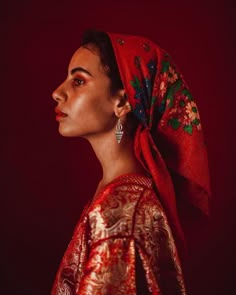 a woman with a red scarf on her head and earrings in front of a dark background