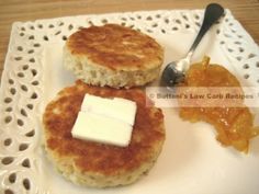 two pancakes with butter and jam on a white plate next to a spoon, sitting on a doily