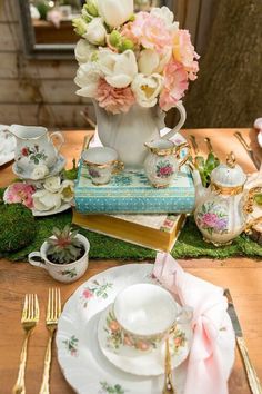 a table set with tea cups, saucers and flowers in vases on top of books