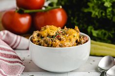 a white bowl filled with some tasty looking food next to tomatoes and celery