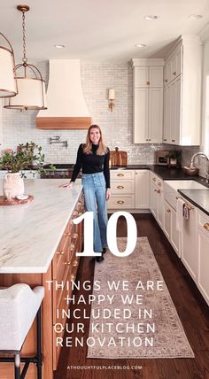 a woman standing in the middle of a kitchen with white cabinets and counter tops, next to an island