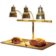 a piece of meat is sitting on a gold plate with three brass lamps above it