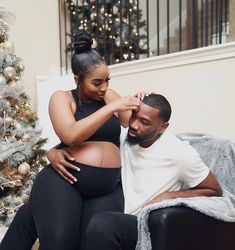 a pregnant couple sitting on a couch in front of a christmas tree