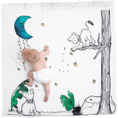 a baby laying on top of a blanket next to a tree with animals and stars