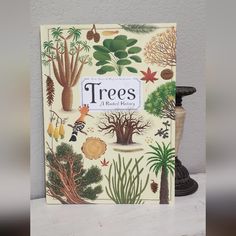 a book with trees on it sitting next to a vase