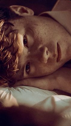 a young man laying on top of a bed next to a white pillow with his eyes closed