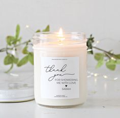 a white candle sitting on top of a table next to a jar with a thank you for showering message