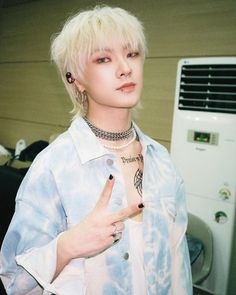 a man with blonde hair and piercings standing in front of an air conditioner