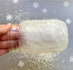 a hand holding a jar filled with sugar and sprinkles on top of snow flakes