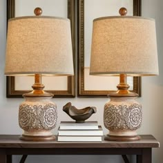 two lamps sitting on top of a wooden table next to a mirror and lamp shade