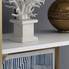 a white vase sitting on top of a white shelf next to a gold bowl filled with flowers