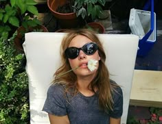 a woman wearing sunglasses and holding a flower in her mouth while sitting on a lawn chair