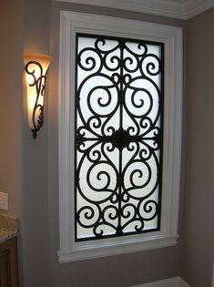 a window with an intricate iron design on it's glass door, in the corner of a room