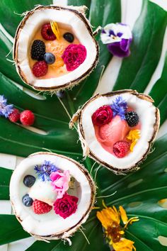 three coconuts filled with fruit and flowers on top of a leafy green plate