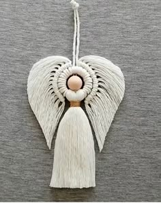 an angel ornament hanging on a gray wall with white tassels and a pink ball in the center