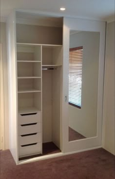 an empty walk in closet with white drawers and mirror on the door, next to a window