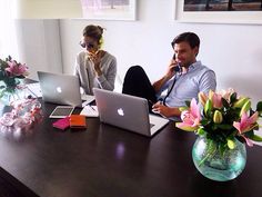 two people sitting at a table with laptops and flowers in front of them on their phones