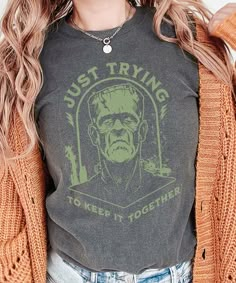 Get ready to keep it spooky and stylish this Halloween with our exclusive 'Just Trying to Keep It Together' Frankenstein Halloween shirt! Perfect for those who love a little Halloween humor, this unique shirt features a distressed Frankenstein design with the quote 'Just Trying to Keep It Together' adorned across the front. Made from soft, high-quality fabric, this shirt offers both comfort and style. Wear it to Halloween parties, trick-or-treating, or simply to celebrate the spirit of the season. Grab yours now and show off your love for Halloween in a fun and fashionable way! Graphic is distressed for a vintage look. Please check the size chart and size up a couple sizes for an oversized look. *The larger the shirt, the larger the graphic.  Our printer sizes the graphics proportionate to