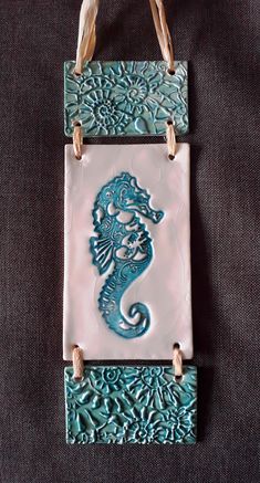 a blue and white tile with a seahorse on it's side, hanging from a rope