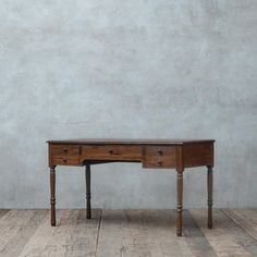 an old wooden desk sitting on top of a hard wood floor next to a wall