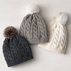 three knitted hats with pom - poms are lined up on a white surface